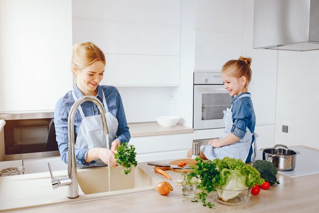 hermosa madre con una camisa azul y un delantal está preparando una ensalada de vegetales frescos en casa