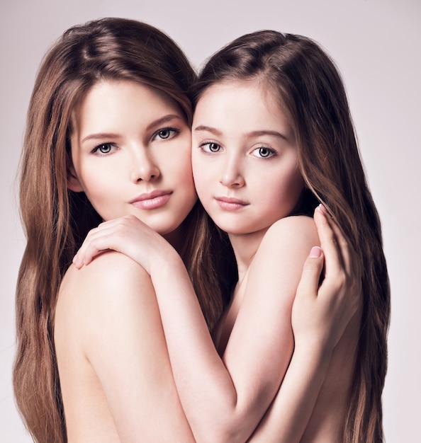 Hermosa madre desnuda e hija pequeña de 8 años con cabello largo castaño se abrazan en el estudio Foto Gratis