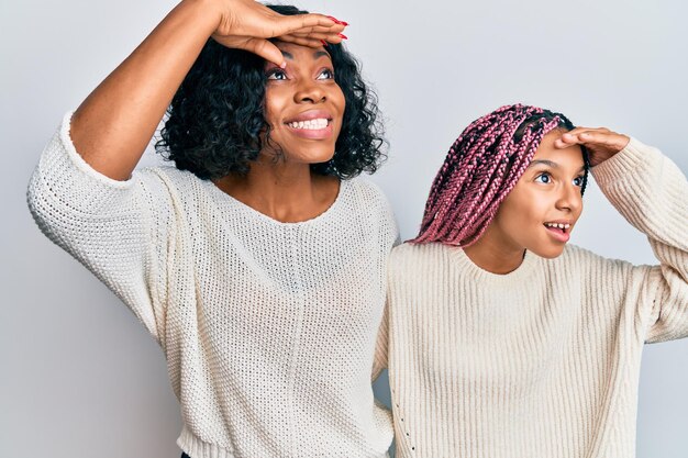 Hermosa madre e hija afroamericanas vestidas con ropa informal y abrazándose muy felices y sonriendo mirando lejos con la mano sobre la cabeza. concepto de búsqueda.