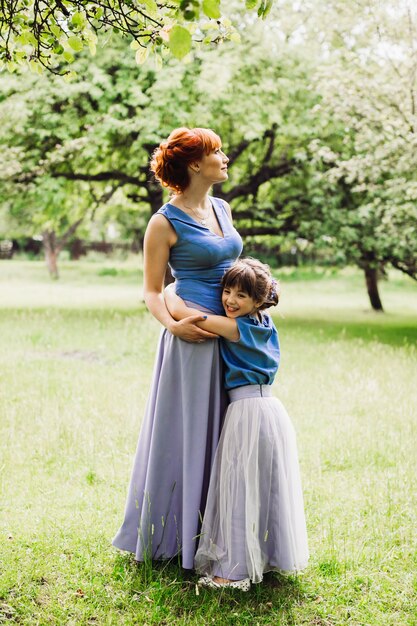 Hermosa madre e hija de pie en el jardín verde