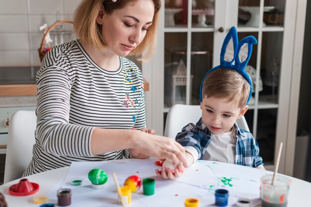 Hermosa madre enseñando a niño a pintar huevos