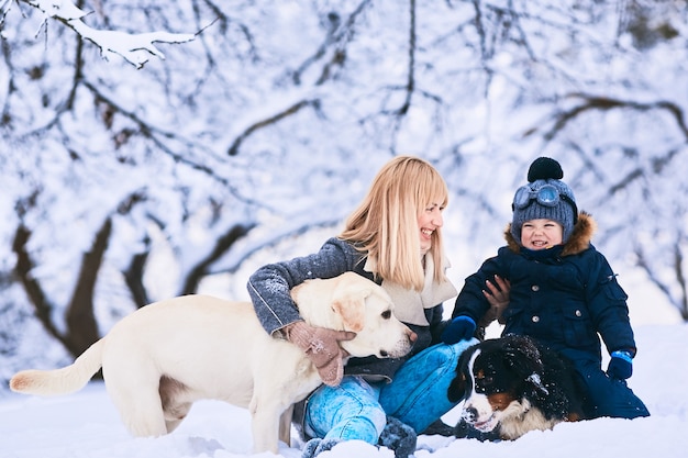 La hermosa madre, hijo y perros sentados en la nieve