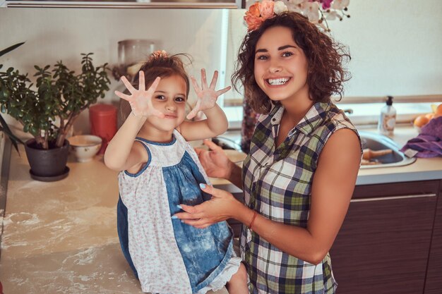 La hermosa madre hispana sonriente y su linda hijita se divierten en la cocina.