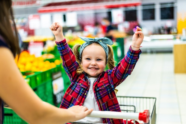 Hermosa madre lleva a su niña en el carrito del supermercado