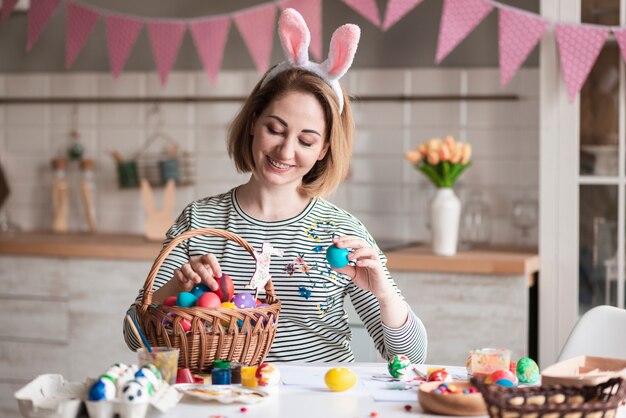 Hermosa madre con orejas de conejo llenando la canasta con huevos