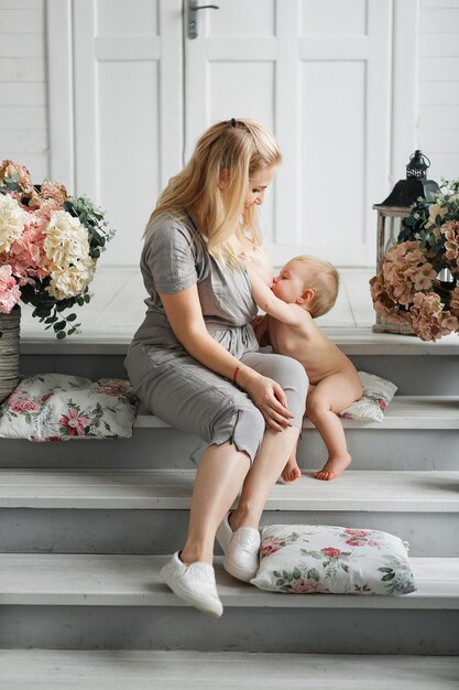 Hermosa madre con pecho grande amamantando a su bebé mientras está sentada en escaleras de madera