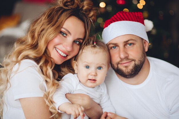 Hermosa madre sonriente y padre con sombrero de Santa abrazando a su hija. Tiempo de Navidad.