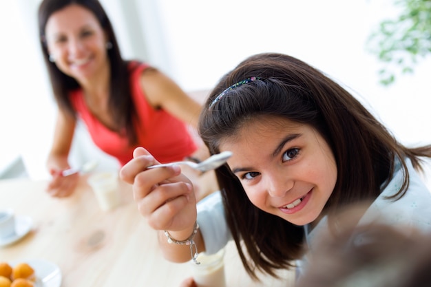 Hermosa madre y su hija comiendo yogurt en casa.