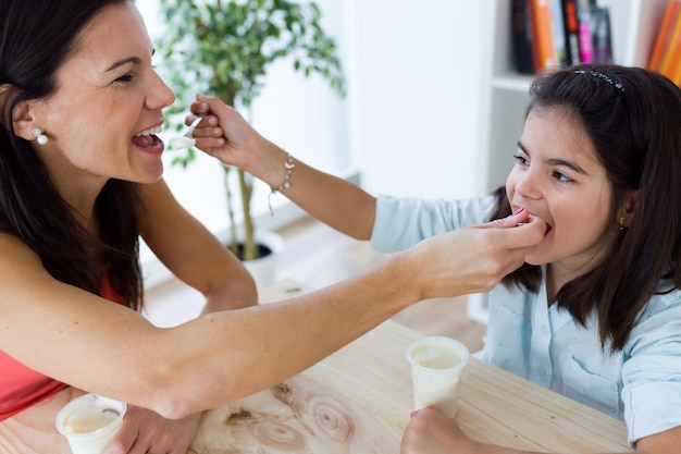 Hermosa madre y su hija comiendo yogurt en casa.