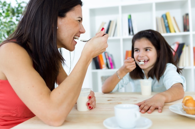 Hermosa madre y su hija comiendo yogurt en casa.