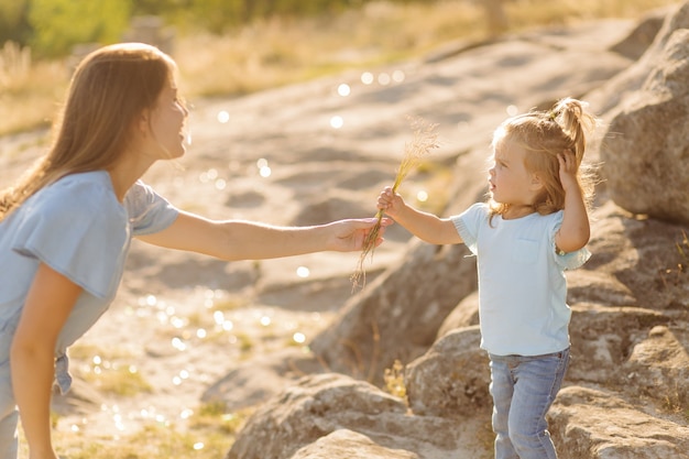 Hermosa madre y su linda hija de pelo largo están caminando sobre una pradera de piedra