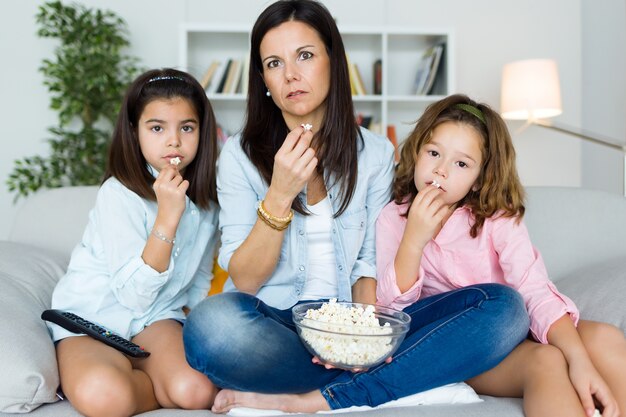 Hermosa madre y sus hijas comiendo palomitas de maíz en casa.