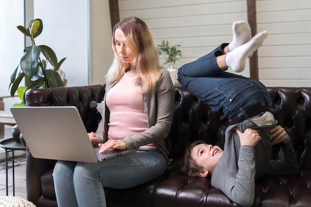 Hermosa madre trabajando junto a su hijo en el sofá