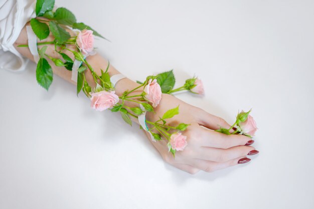 Una hermosa mano femenina delgada se encuentra con flores rosas sobre un fondo blanco.