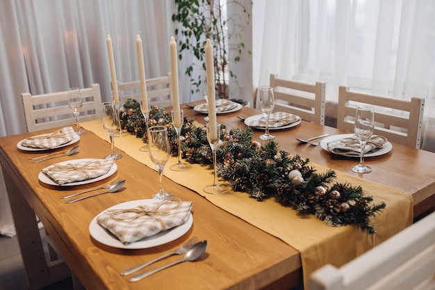 Hermosa mesa de servir de Navidad con velas y decoración de abeto en primer plano interior moderno y acogedor. Celebrando las vacaciones de diciembre, el año nuevo, rodeado de platos y vasos decorados de temporada.