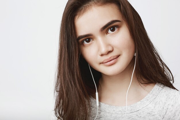 hermosa modelo europea sonriendo con labios apretados, escuchando música en auriculares