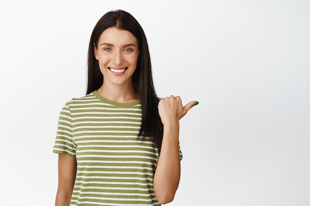 Hermosa modelo femenina sonriente apuntando a la derecha mostrando el anuncio de venta de la tienda en el espacio en blanco vacío de fondo blanco