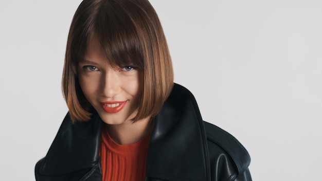 Foto gratuita hermosa modelo de moda con cabello bob y labios rojos mirando con confianza a la cámara y sonriendo sobre fondo blanco