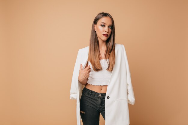 Hermosa modelo de mujer con cabello largo castaño claro y labios de vid posando en una pared aislada con una sonrisa encantadora. Retrato de joven bien arreglada con primer plano de piel perfecta