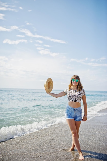 Foto gratuita hermosa modelo relajándose en una playa de mar usando jeans, camisa corta de leopardo y sombrero