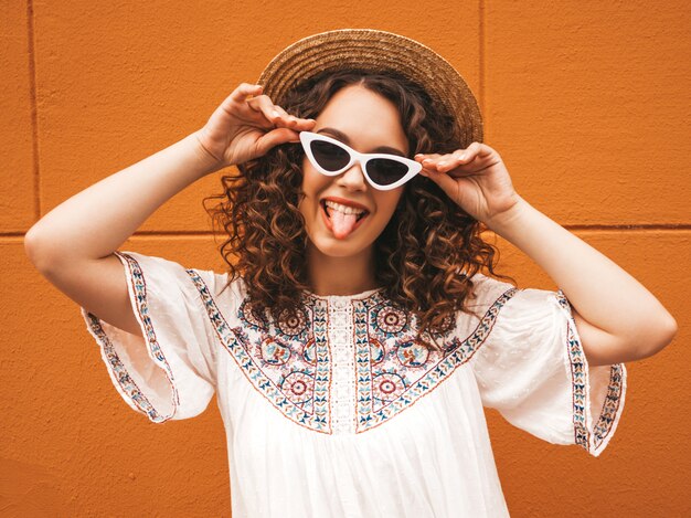 Hermosa modelo sonriente con peinado afro rizos vestido con vestido blanco hipster de verano y gafas de sol