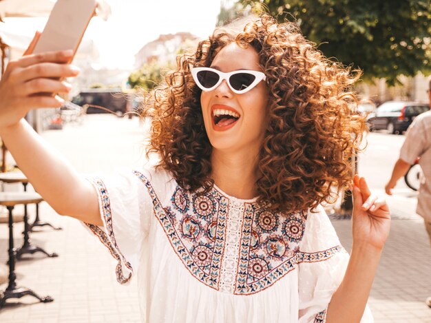 Hermosa modelo sonriente con peinado afro rizos vestido con vestido blanco hipster de verano.