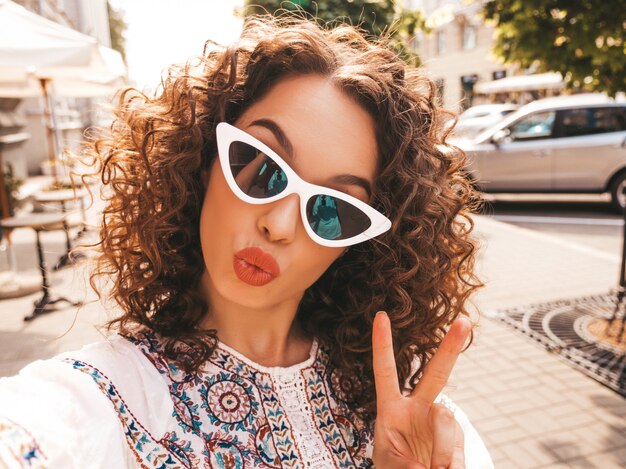 Hermosa modelo sonriente con peinado afro rizos vestido con vestido blanco hipster de verano.