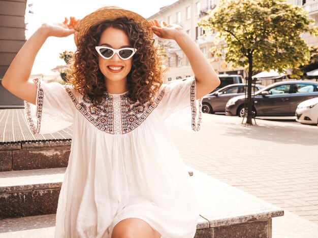 Hermosa modelo sonriente con peinado afro rizos vestido con vestido blanco hipster de verano.