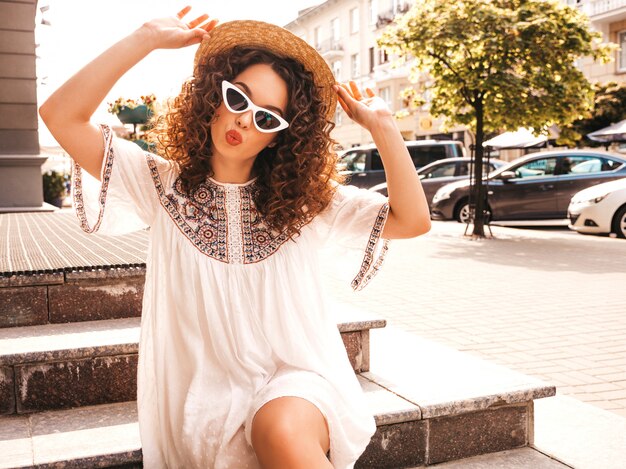 Hermosa modelo sonriente con peinado afro rizos vestido con vestido blanco hipster de verano.