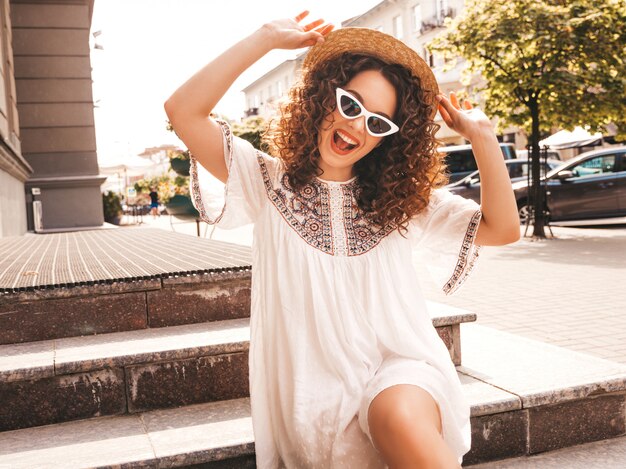 Hermosa modelo sonriente con peinado afro rizos vestido con vestido blanco hipster de verano.