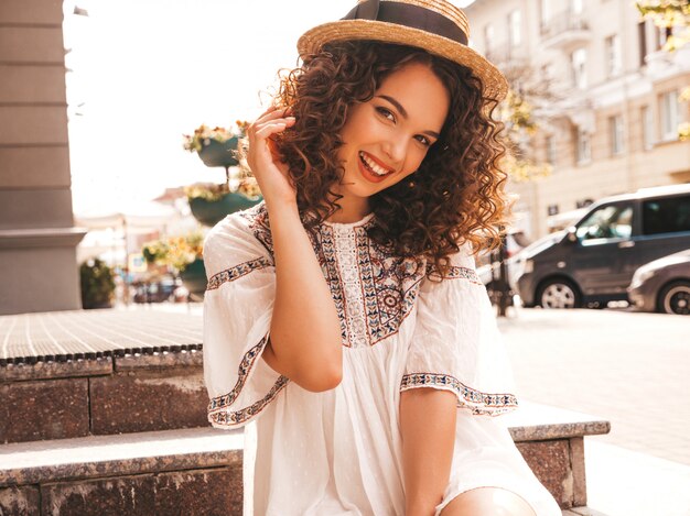 Hermosa modelo sonriente con peinado afro rizos vestido con vestido blanco hipster de verano.