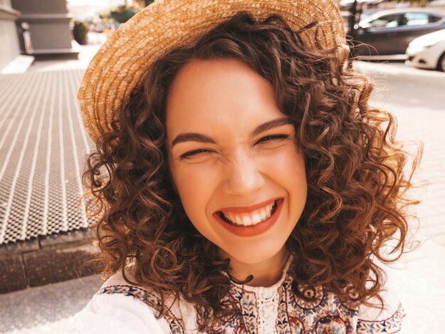 Hermosa modelo sonriente con peinado afro rizos vestido con vestido blanco hipster de verano.