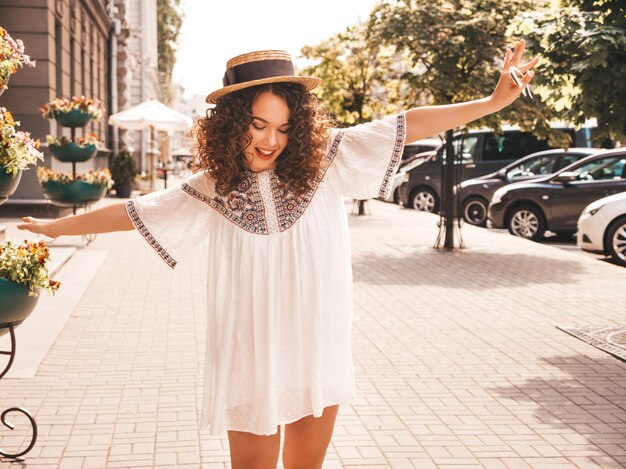 Hermosa modelo sonriente con peinado afro rizos vestido con vestido blanco hipster de verano.