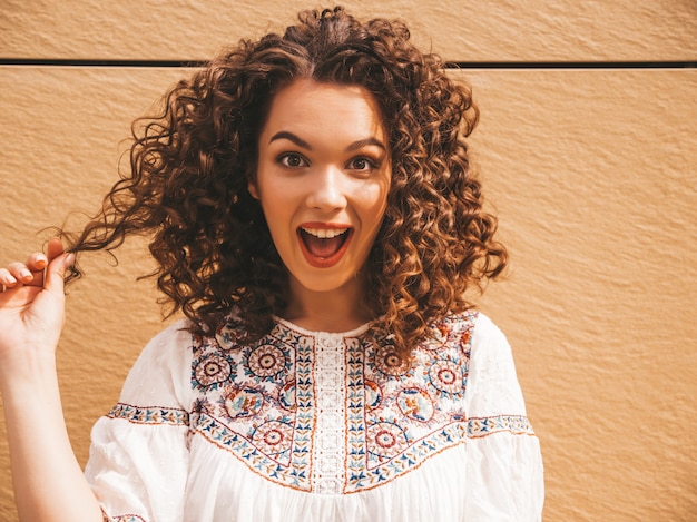 Hermosa modelo sonriente con peinado afro rizos vestido con vestido blanco hipster de verano.