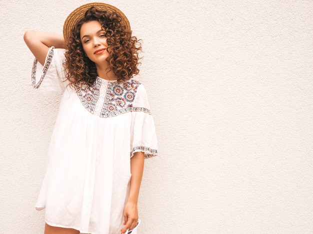 Hermosa modelo sonriente con peinado afro rizos vestido con vestido blanco hipster de verano.