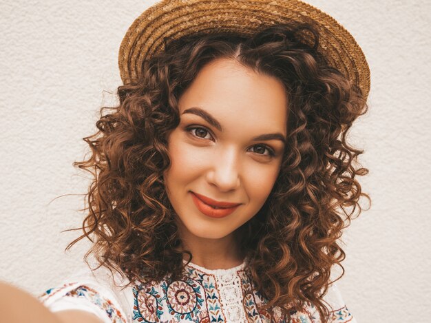 Hermosa modelo sonriente con peinado afro rizos vestido con vestido blanco hipster de verano.