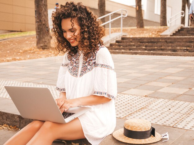 Hermosa modelo sonriente con peinado afro rizos vestido con vestido blanco hipster de verano.