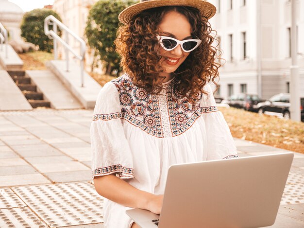 Hermosa modelo sonriente con peinado afro rizos vestido con vestido blanco hipster de verano.