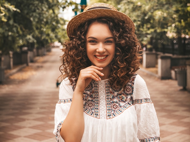 Hermosa modelo sonriente con peinado afro rizos vestido con vestido blanco hipster de verano.