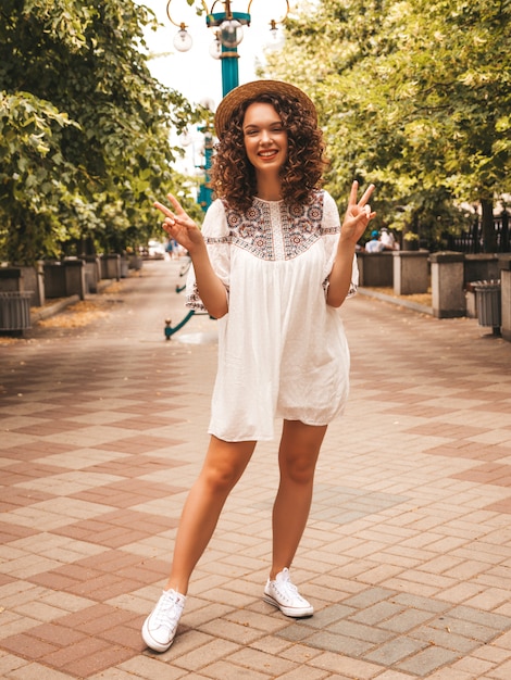 Hermosa modelo sonriente con peinado afro rizos vestido con vestido blanco hipster de verano.