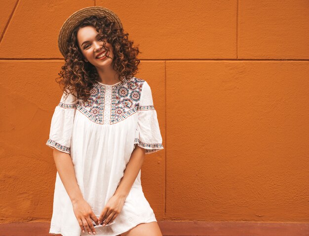 Hermosa modelo sonriente con peinado afro rizos vestido con vestido blanco hipster de verano.