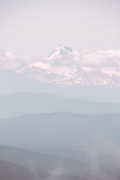 Hermosa montaña cubierta de nieve y rodeada de nubes durante un clima brumoso