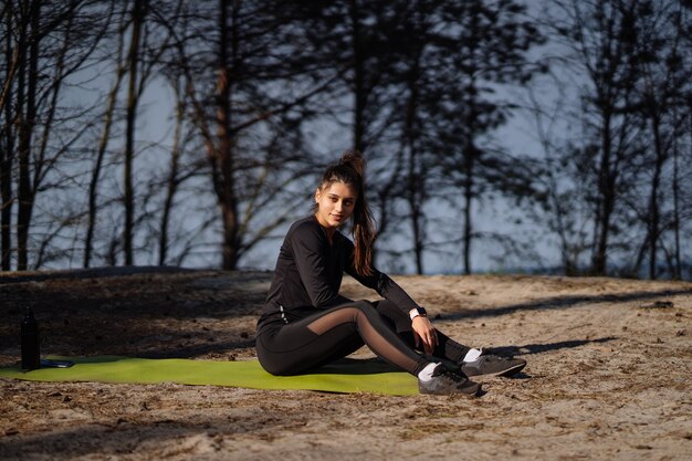 Hermosa morena cucasiana vestida con ropa deportiva sentada en la estera en la naturaleza