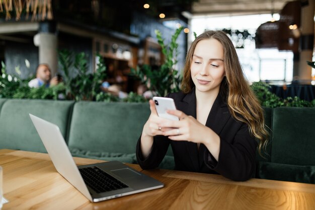 Hermosa morena con ordenador portátil y teléfono móvil en la cafetería. Concepto de trabajo de Blogger