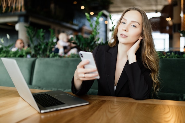 Hermosa morena con ordenador portátil y teléfono móvil en la cafetería. Concepto de trabajo de Blogger