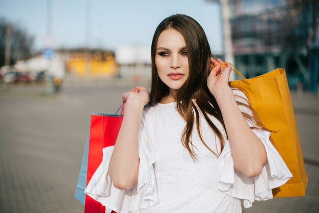 Hermosa morena con el pelo largo se encuentra con bolsas de compras antes de un moderno edificio de vidrio