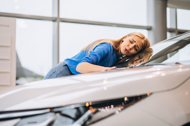 Hermosa mujer abrazando un automóvil en un showrrom de automóviles