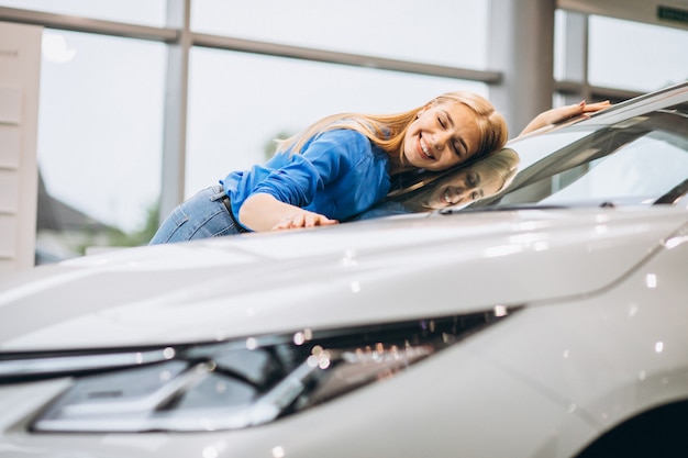 Hermosa mujer abrazando un automóvil en un showrrom de automóviles