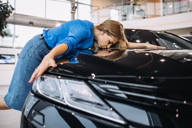 Hermosa mujer abrazando un automóvil en un showrrom de automóviles