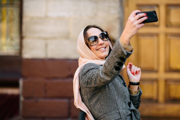 Hermosa mujer con un abrigo en la calle hace selfie